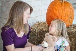 A woman gives a teddy bear to a happy child.