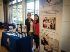 Two business women stand ready to greet visitors at a conference booth.