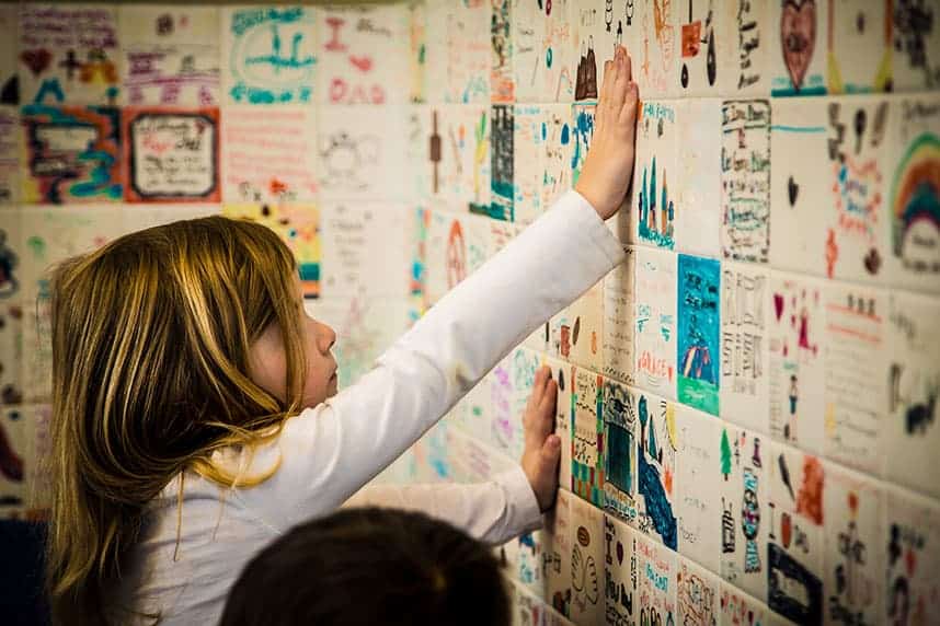 A young girl places her hand on a memorial wall, remembering a loved one.