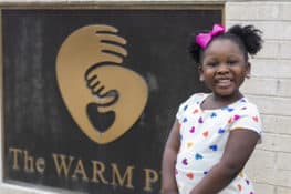 A young girl stands in front of The WARM Place smiling