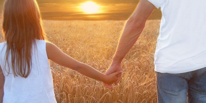 Father with his daughter at sunset in barley field