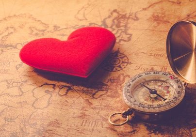 Valentine day background. Old compass on vintage map with red heart. Retro filter. Direction to real love of your heart concept.